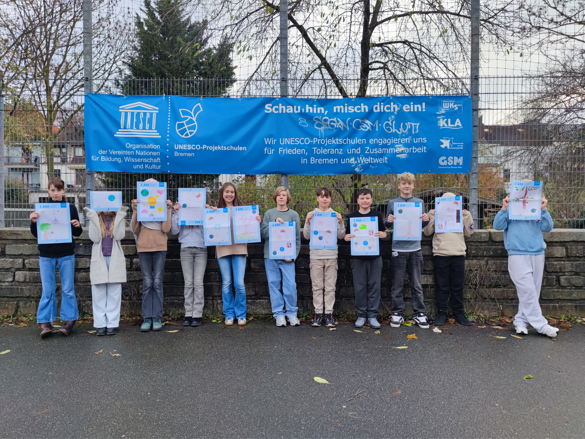 Gruppe von Kindern steht vor einer Mauer mit blauem Banner und hält Plakate mit bunten Punkten hoch